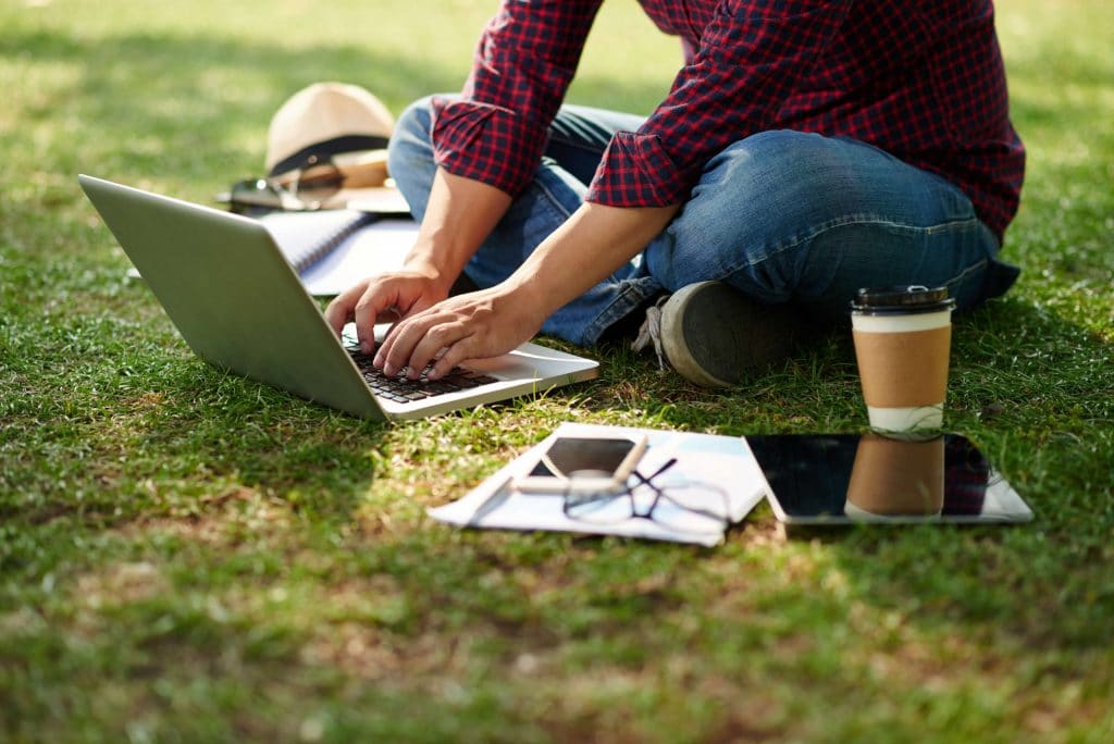 Kvinna som undersöker lån för studenter på sin laptop medan hon sitter i gräset.