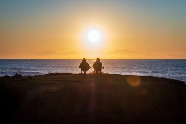 Ett par njuter av sin pension genom att titta på solnedgången tillsammans, symboliserande ett bekymmersfritt äldre liv.