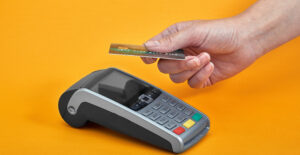 närbild av knapparna på en betalningsmaskin med en mänsklig hand som håller ett plastkort nära på gul bakgrund vid avbetalning.