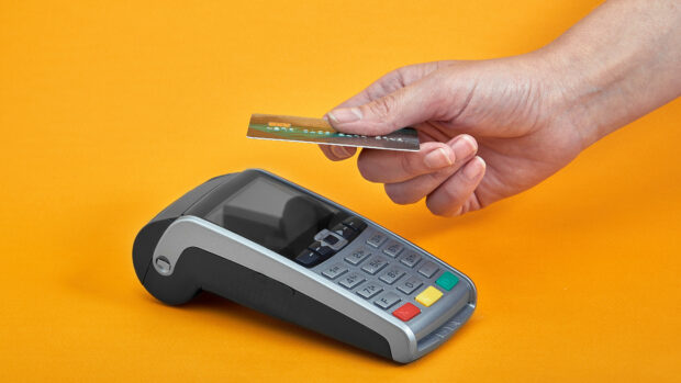 Närbild av knapparna på en betalningsmaskin med en mänsklig hand som håller ett plastkort nära på gul bakgrund vid avbetalning