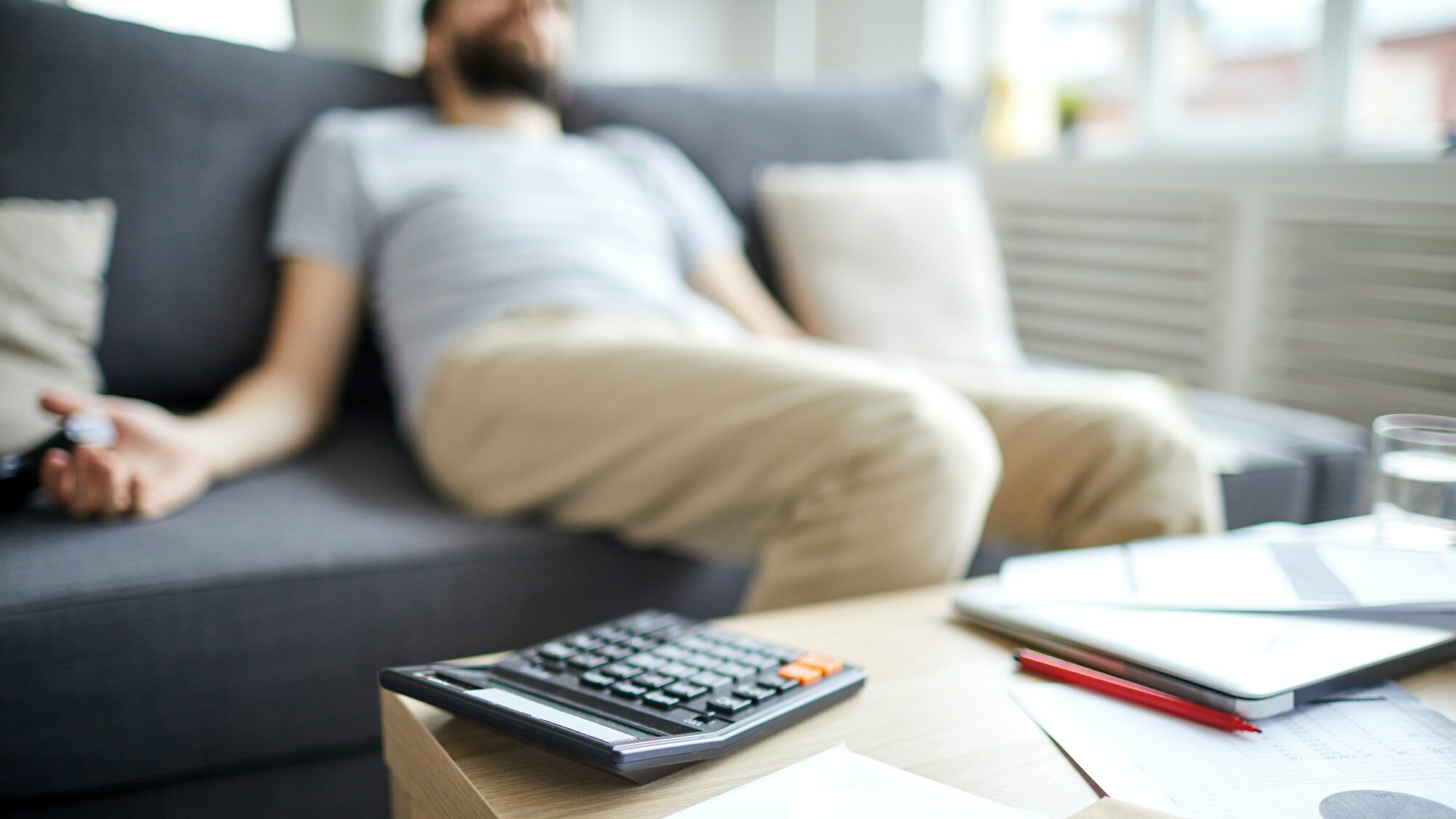 Man ser trött ut sittandes i en soffa med en miniräknare i handen, bekymrad över att beräkna sin skuldkvot.
